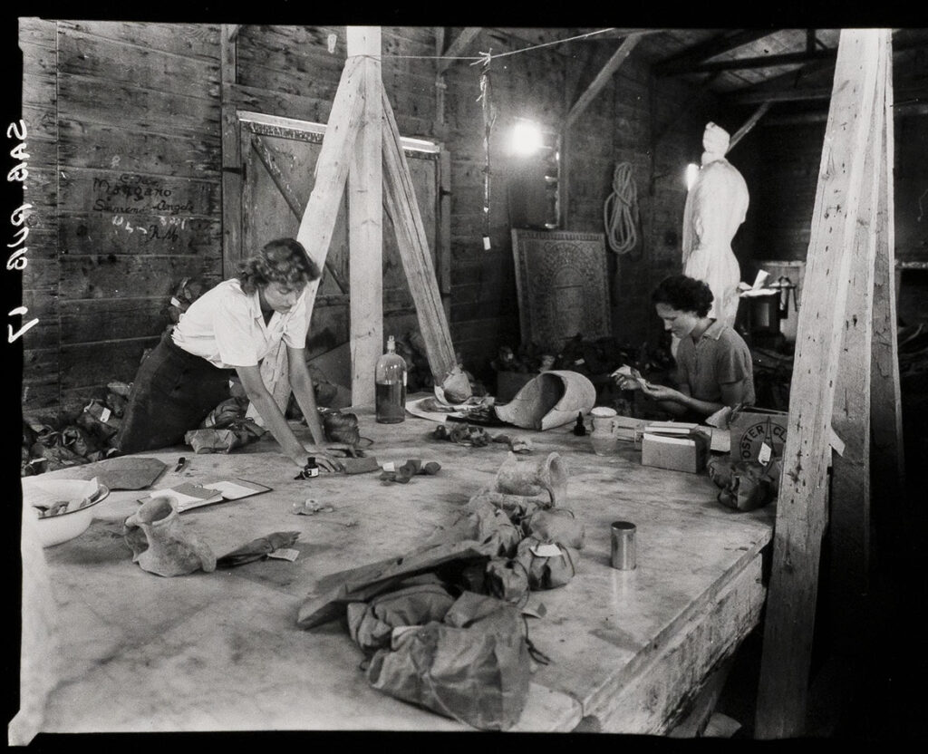 A black and white photograph of two people labelling ceramic finds.